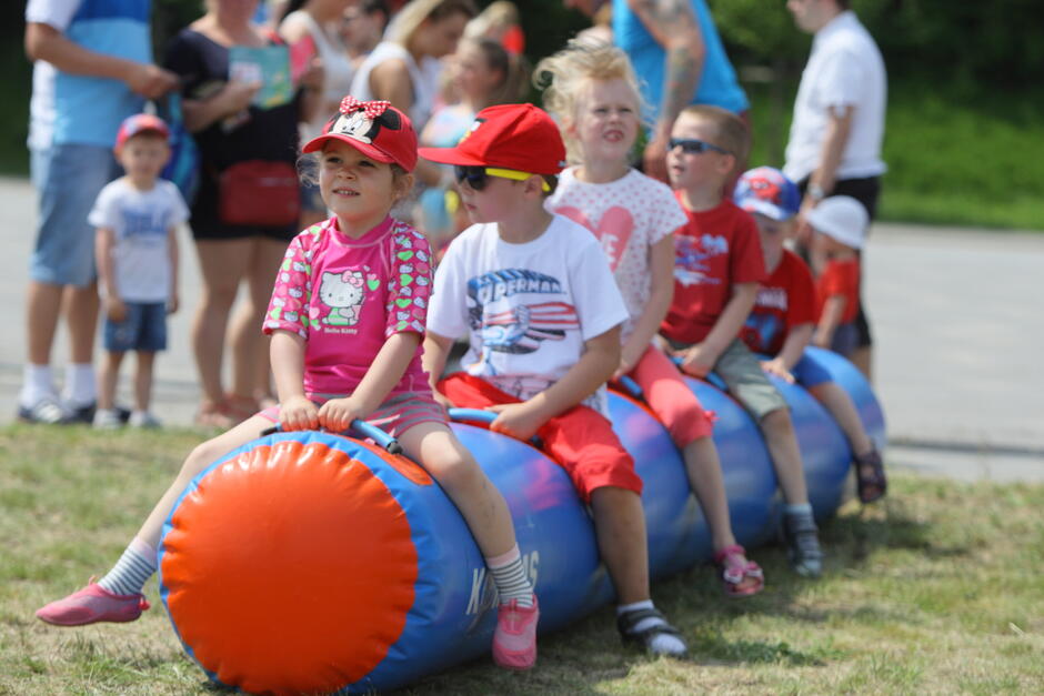 na zdjęciu kilkoro małych dzieci, siedzą na dmuchanej rurze, jedno za drugim