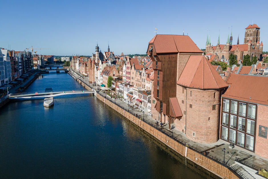 na zdjęciu z drona, po prawej widać zabytkową zabudowę gdańska, w tym kamienice ceglane i dawny żuraw, po lewej płynie rzeka