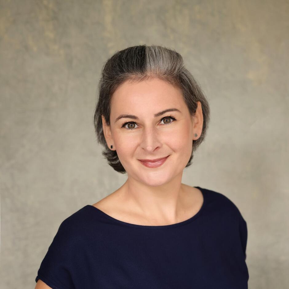 Na zdjęciu kobieta w krótkich włosach, za uszy, w ciemnej koszulce.