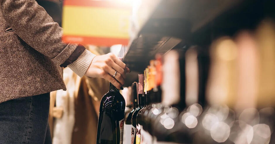Ręka sięga po butelkę wina na półce z alkoholami.