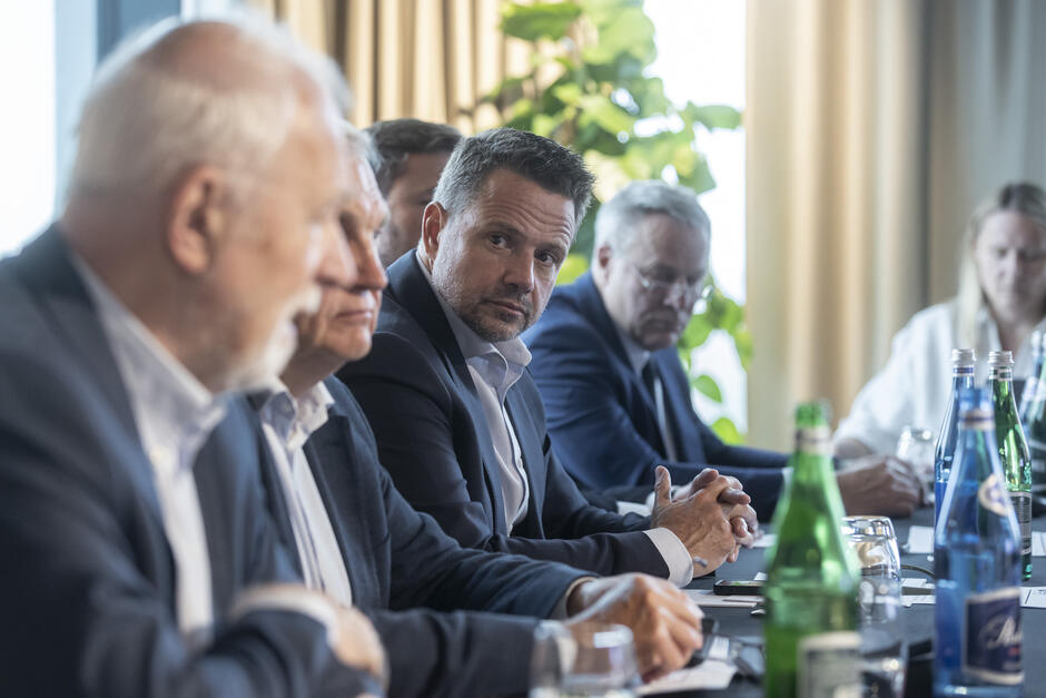 Kilka osób siedzi przy stole obrad - centralnie wśród nich widoczny jest Rafał Trzaskowski 