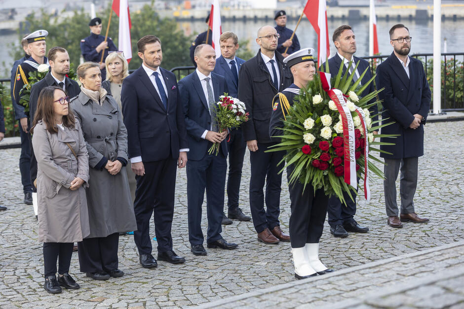 Grupa osób z kwiatami, u stóp pomnika
