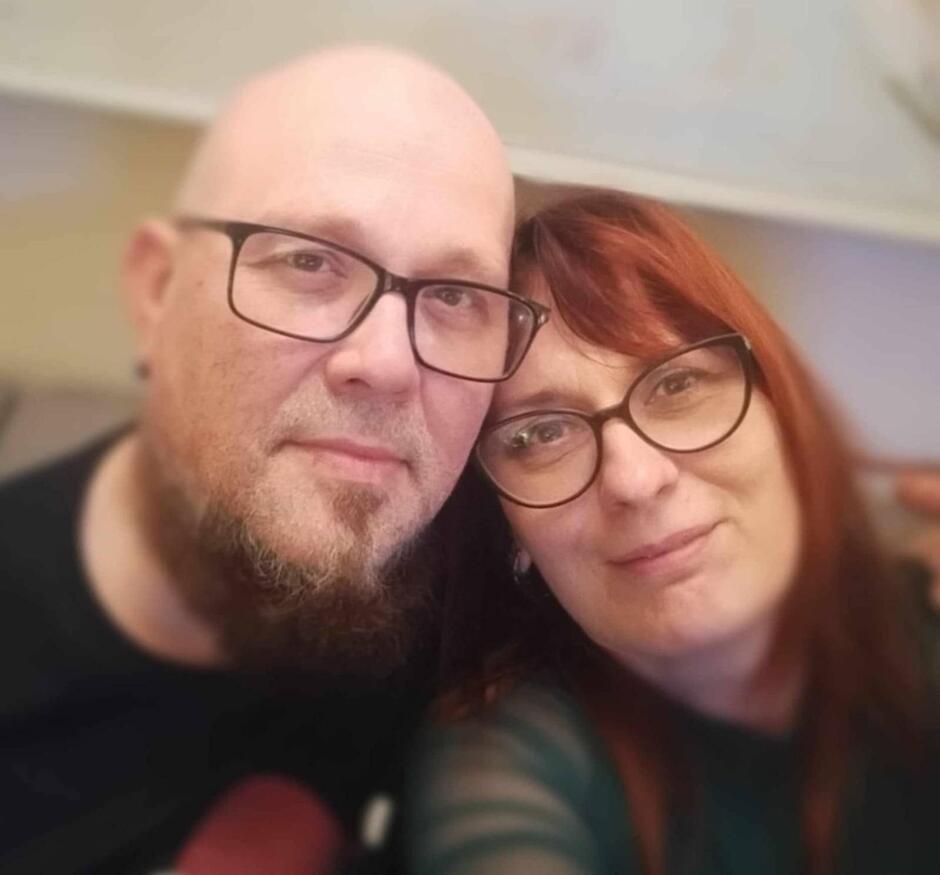 od lewej łysy mężczyzna z brodą i w okularach, obok kobieta w okularach z włosami za ramiona.  