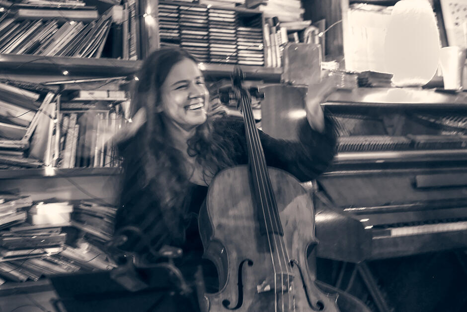 Kobieta z długimi włosami, trzymająca instrument smyczkowy na tle książek.