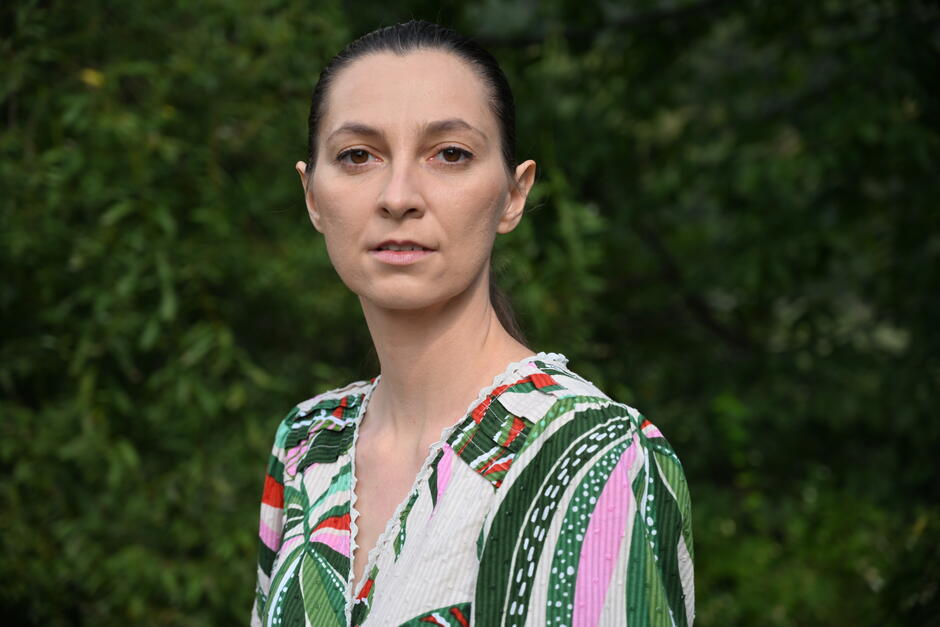 kobieta o ciemnych włosach, w kolorowej bluzce, na tle zieleni