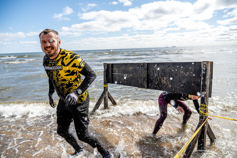 Mężczyzna biegnie w biegu terenowym, pokonując przeszkodę w morzu.