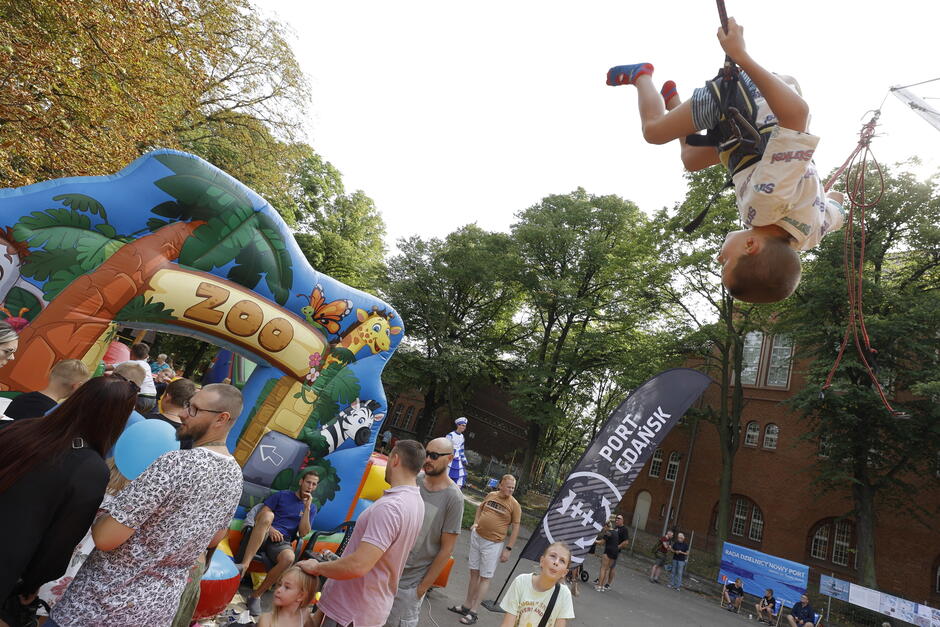 na zdjęciu chłopiec skaczący na linie i robiący w powietrzu fikołka, przyglądają mu się inne dzieci