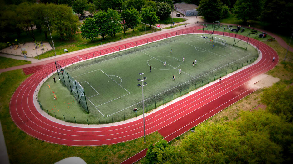 widok z lotu ptaka na boisko o zielonej nawierzchni, wokół niego widać czerwoną bieżnię do biegania
