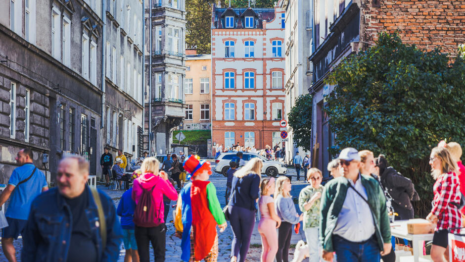 grupa kolorowo ubranych ludzi stoi na ulicy w otoczeniu zabytkowych kamienic