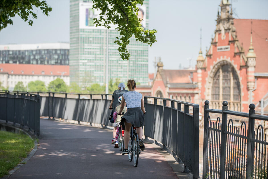 na zdjęciu dwoje rowerzystów, jadą tyłem do fotografującego, po prawej fragmenty zabytkowych budynków