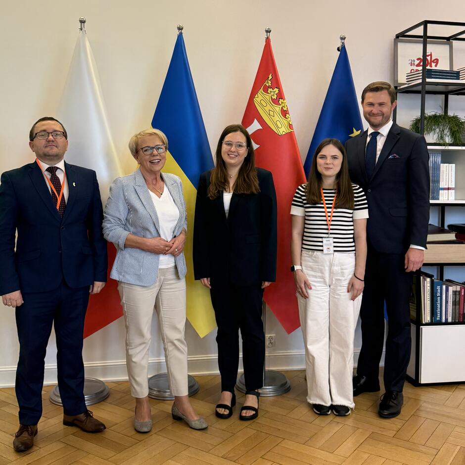 Wspólne zdjęcie pięciu osób na tle stojących flag Polski, Ukrainy, Gdańska i Unii Europejskiej