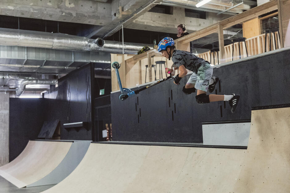 Chłopak w kasku wykonuje ewolucję na hulajnodze w skateparku.