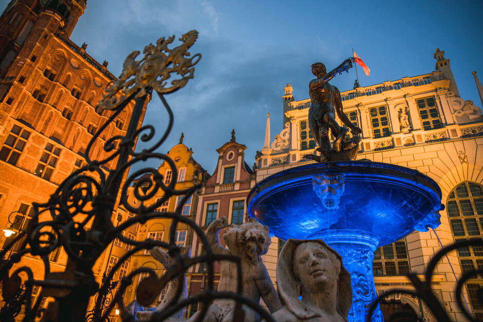 Sfotografowana od dołu fontanna Neptuna. Misa pod rzeźbą Neptuna podświetlona jest w kolorze intensywnie niebieskim 