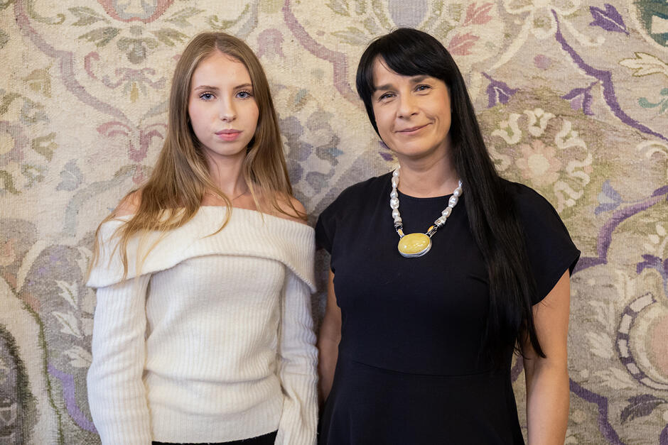 Dwie kobiety pozują do zdjęcia w zdobnej sali.