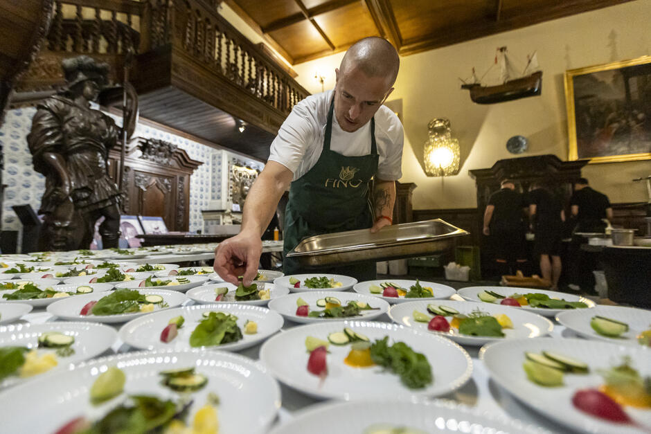 W reprezentacyjnej sali kucharz układa na talerzach zieleninę.