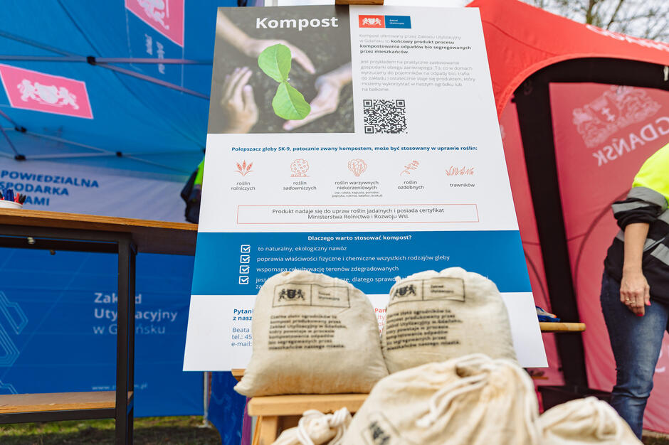 Na zdjęciu znajduje się zestaw pięciu pojemników do segregacji odpadów: niebieski na papier, żółty na metale i tworzywa sztuczne, zielony na szkło, brązowy na bioodpady i szary na odpady resztkowe. Każdy kosz ma wyraźną etykietę z przykładami odpadów, które można do niego wrzucać.
