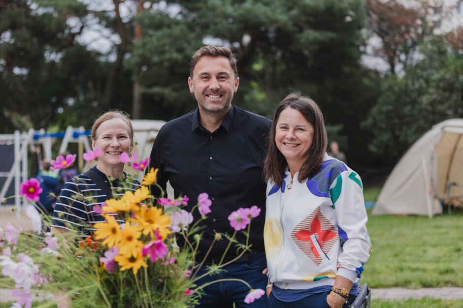 Dwie kobiety i jeden mężczyzna pozują do zdjęcia w parku podczas festynu dzielnicowego.