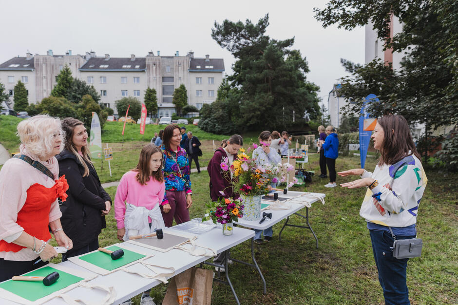 Kilka osób stoi przy stolikach, przy których odbywają się warsztaty w parku podczas festynu dzielnicowego.