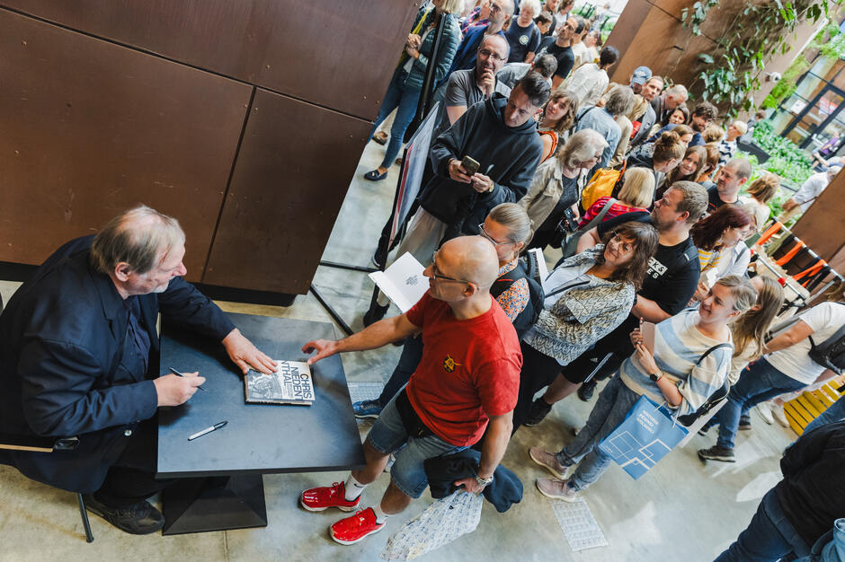 Po lewej autor przy biurku - po prawej długa kolejka fanów