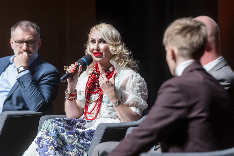 Cztery osoby siedzą w fotelach na scenie, dyskutują