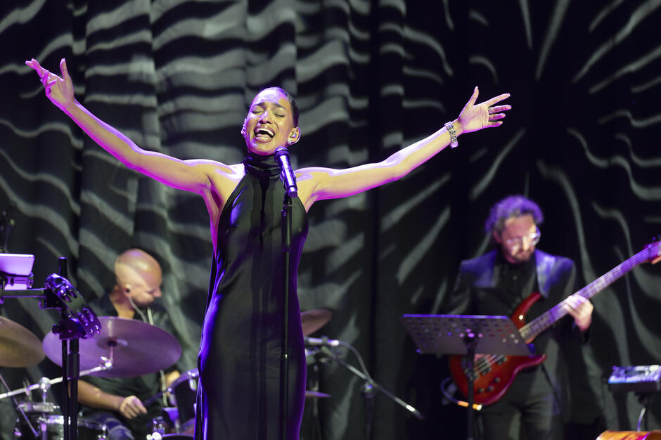 Kobieta śpiewa na scenie z zespołem.