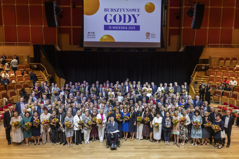 Kilkadziesiąt osób pozuje do fotografii w sali koncertowej.