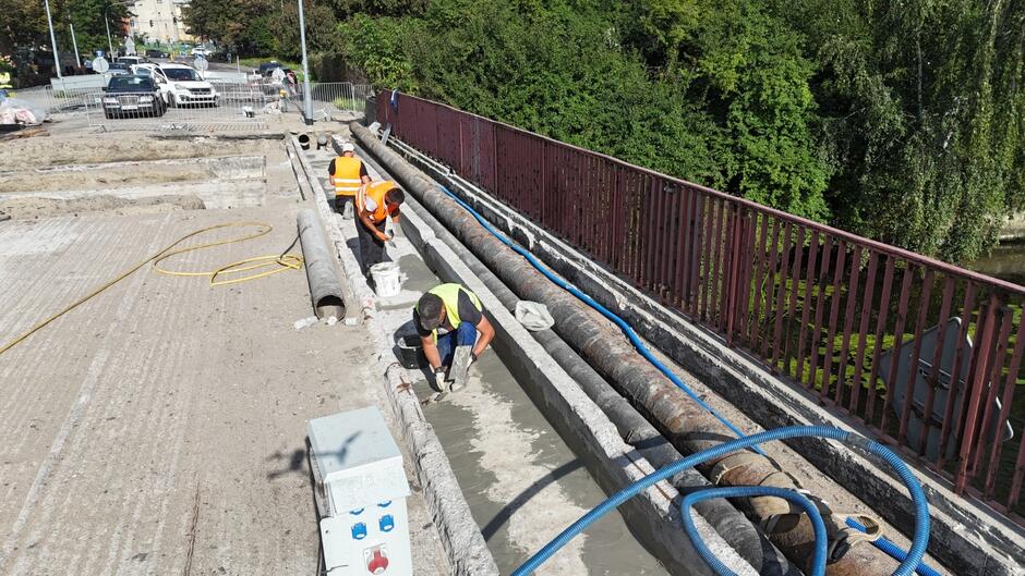 na zdjęciu remontowany most, poi prawej trzech robotników przy pracy