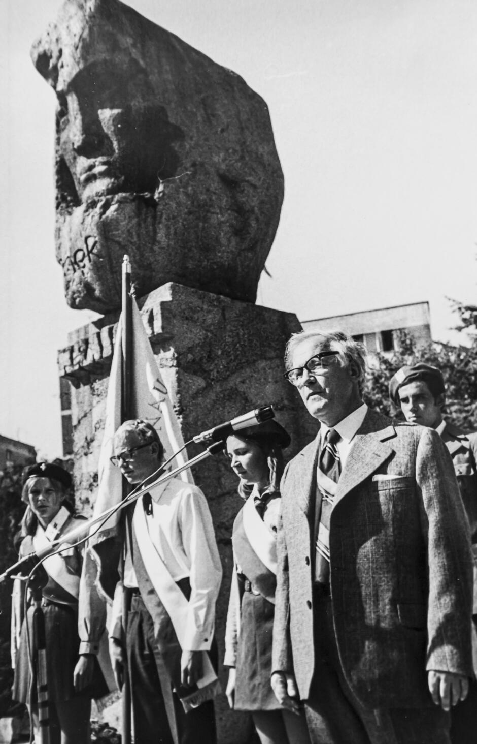 czarnobiałe zdjęcie grupy ludzi stojących pod kamiennym pomnikiem. 