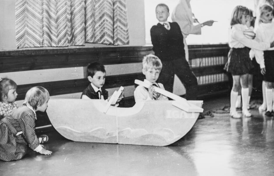 czarnobiałe zdjęcie dzieci w trakcie przedstawienia. Dwóch chłopców udaje, że płynie w łódce