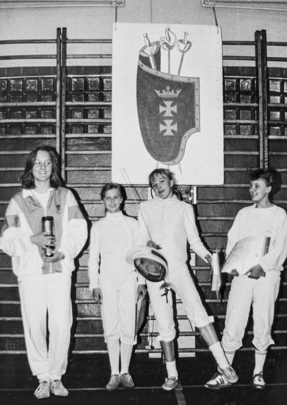 grupa dziewcząt pozuje do zdjęcia w strojach do szermierki i szpadami w dłoniach