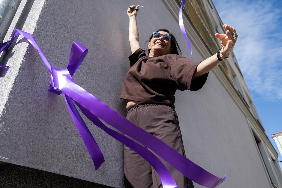 Kobieta z nożyczkami cieszy się po przecięciu wstęgi i odsłonięciu muralu.
