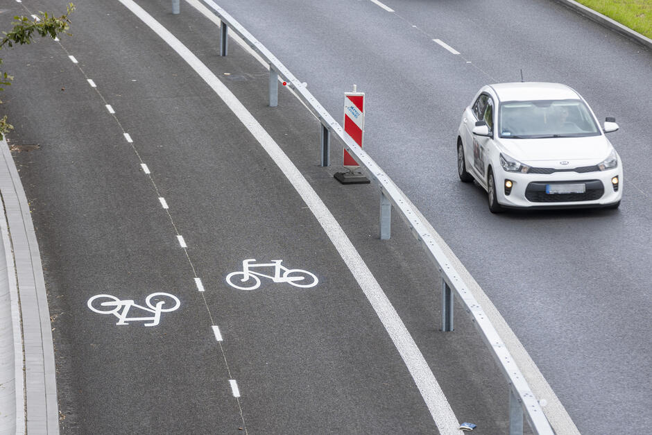 zdjęcie z drona, po lewej widać oznakowaną drogę rowerową, po prawej jezdnię i jadący samochód