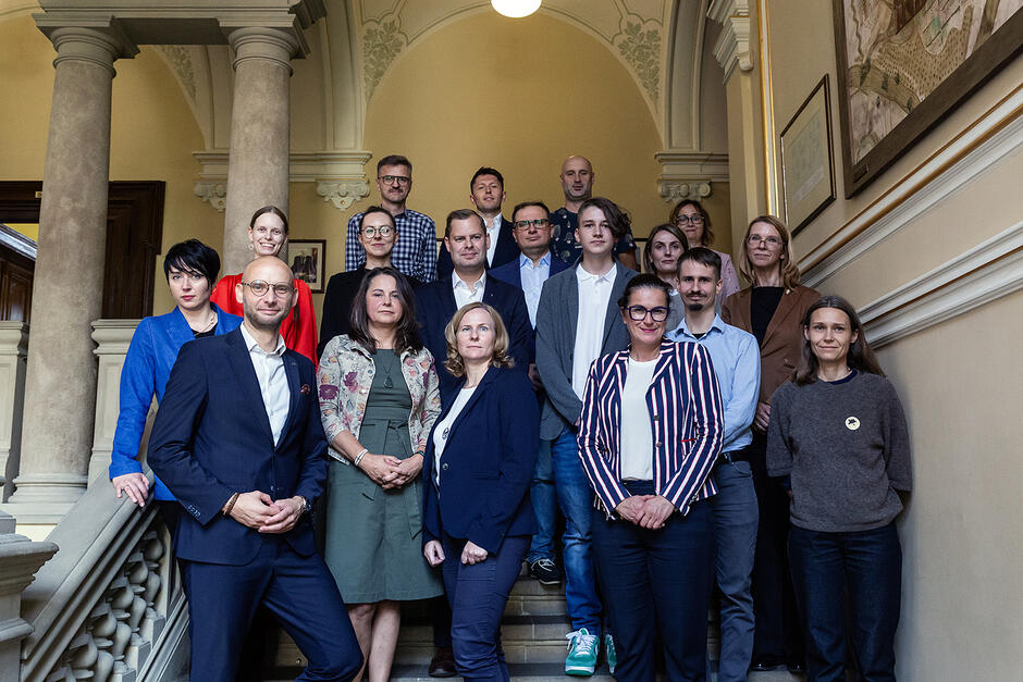Grupa kilkunastu osób pozuje do zdjęcia stojąc na schodach reprezentacyjnego hallu. 