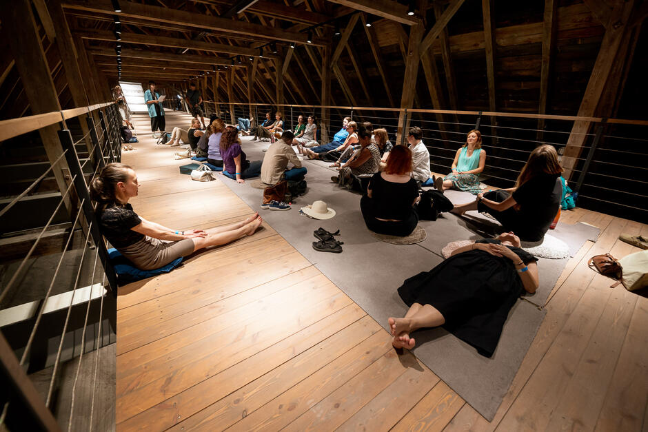 Drewniane poddasze gotyckiego kościoła. Na drewnianej podłodze siedzą i leżą ludzie.