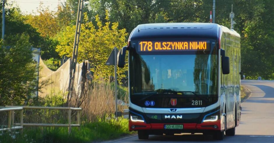 Na zdjęciu widać nowoczesny autobus linii 178 z napisem „Olszynka Niwki” na tablicy kierunkowej. Pojazd jedzie w słoneczny dzień w otoczeniu zieleni i drzew.
