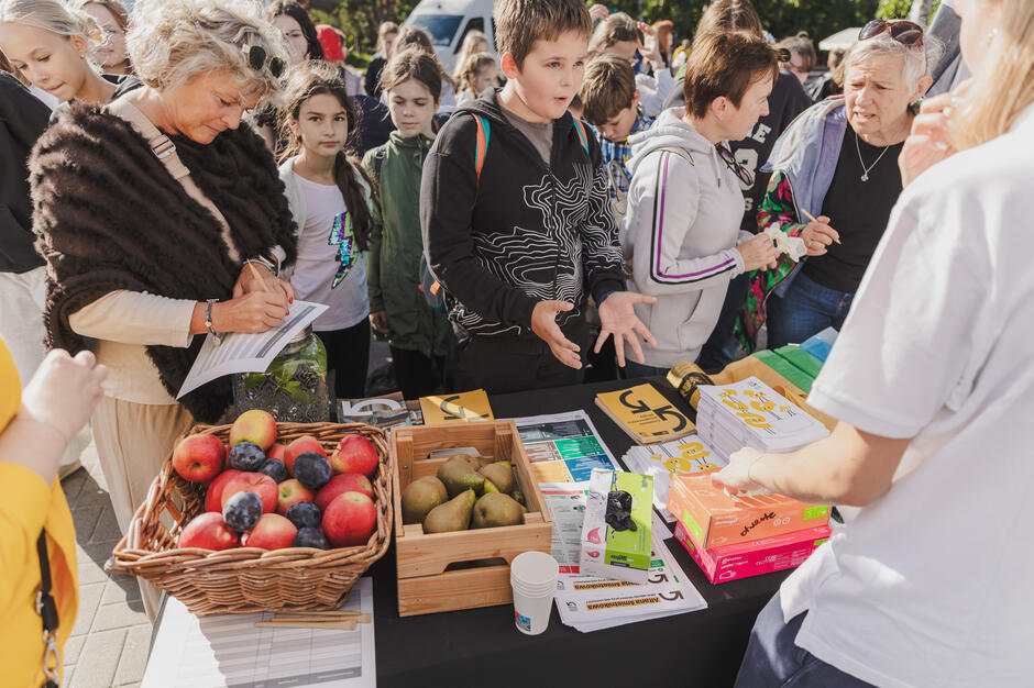 Na zdjęciu grupa wolontariuszy w niebieskich koszulkach pozuje wspólnie podczas akcji „Czyste Miasto Gdańsk”, trzymając worki na śmieci i chwytaki do odpadów. W tle widoczny jest biały namiot organizacyjny oraz flagi, co podkreśla oficjalny charakter wydarzenia.
