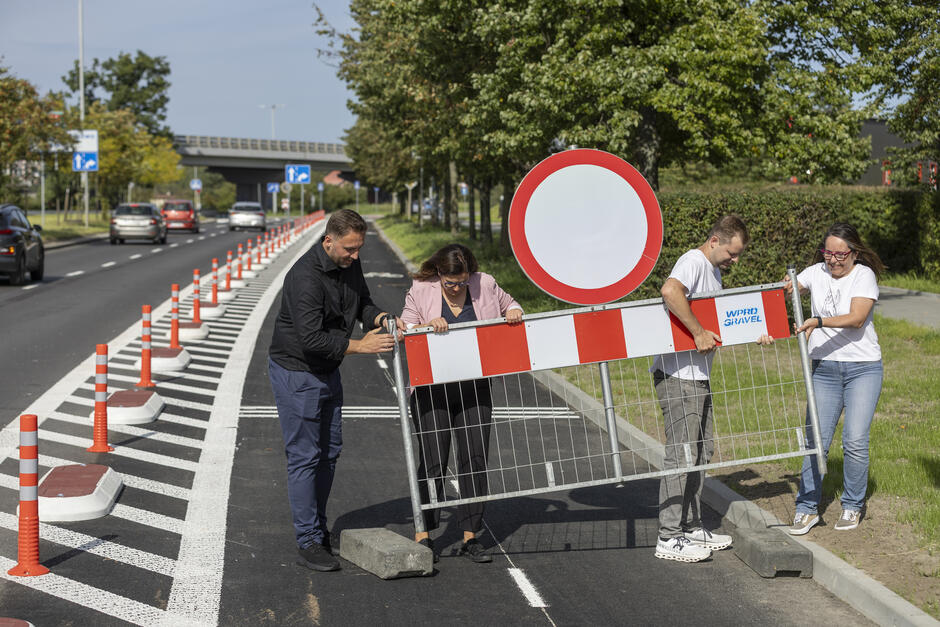 na zdjęciu dwie kobiety i dwóch mężczyzn podnoszą stalową barierkę drogową i przenoszą ją na trawnik