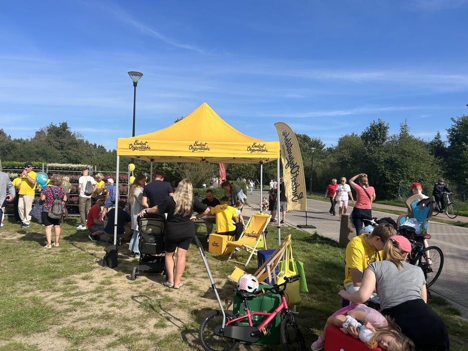 na zdjęciu fragment pikniku widać żółty namiot, sporo ludzi, jedni stoją, inni siedzą