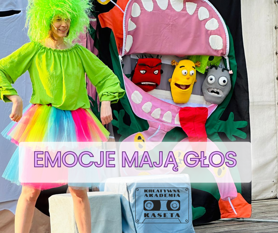 Osoba w kolorowym stroju stoi obok dekoracji z pacynkami przedstawiającymi różne emocje; na obrazie widnieje napis „Emocje mają głos”.