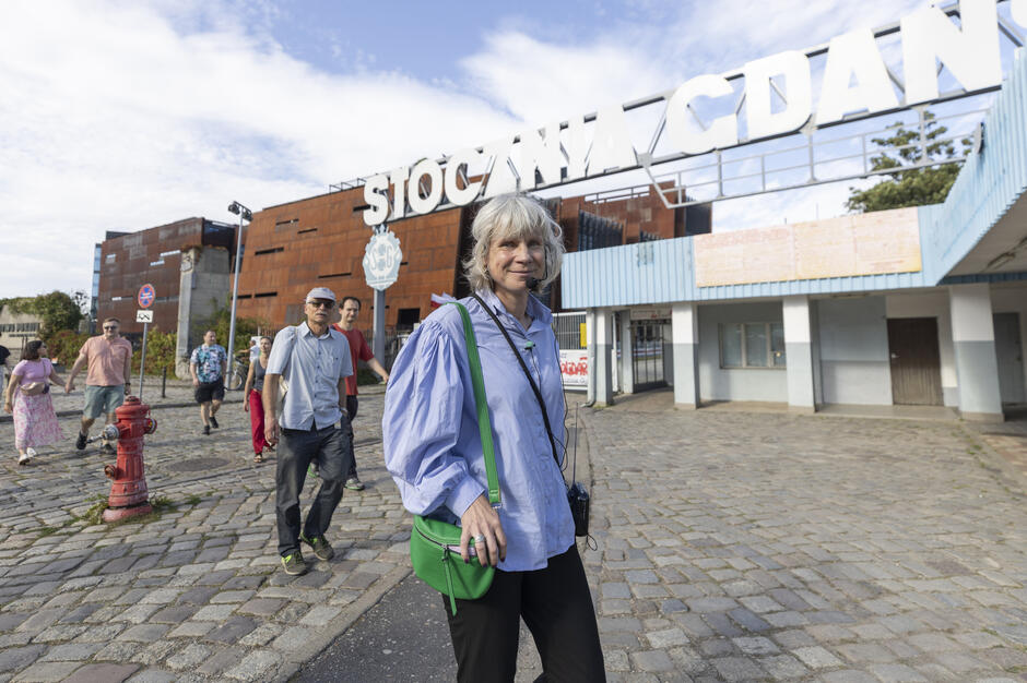 Kobieta prowadzi grupę ludzi w czasie spaceru po terenach po stoczniowych.