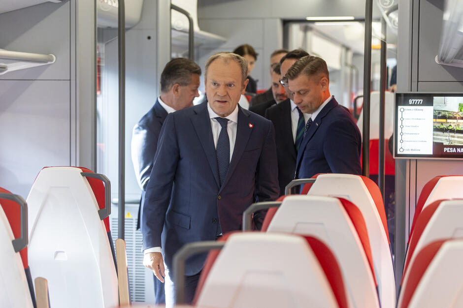 grupa elegancko ubranych mężczyzn sfotografowana we wnętrzu pociągu osobowego