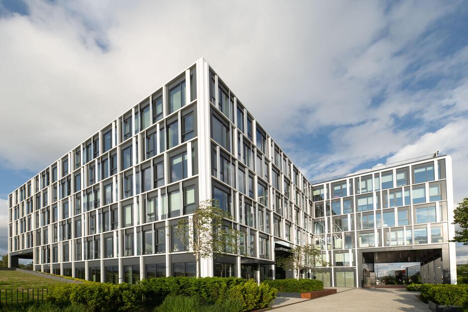 Nowoczesny biurowiec, przed którym rośnie zieleń.