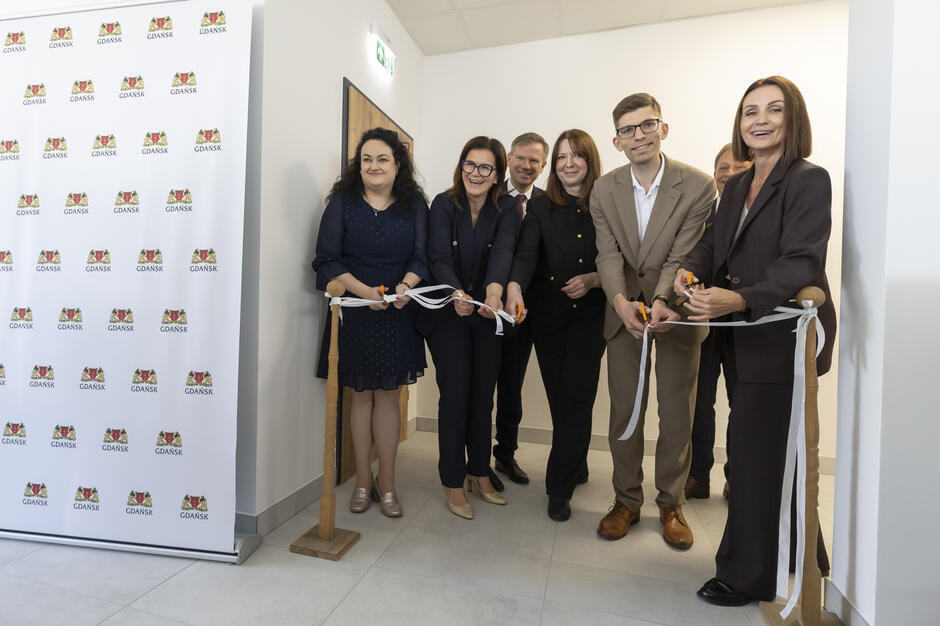 Kilka osób przecina wstęgę w budynku podczas jego otwarcia.