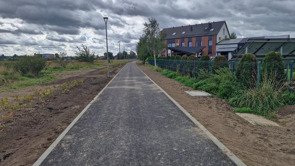 na zdjęciu ciemna droga rowerowa, po prawej widać niewysoki podłużny budynek prawdopodobnie mieszkalny