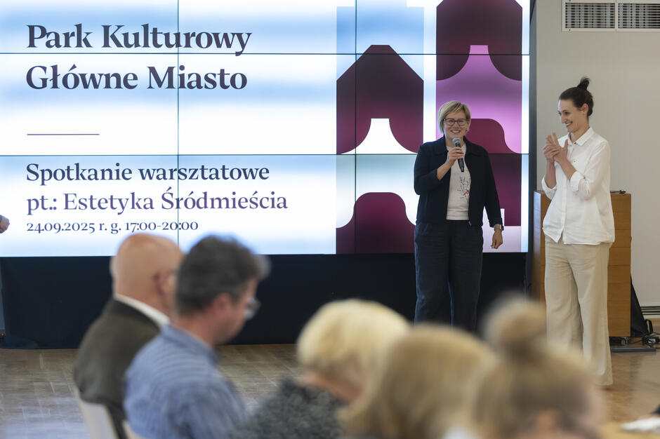 Na zdjęciu widać prowadzące spotkanie warsztatowe pt. „Estetyka Śródmieścia” organizowane w ramach Parku Kulturowego Główne Miasto. W tle wyświetlany jest ekran z informacją o wydarzeniu, a na pierwszym planie siedzą uczestnicy spotkania.
