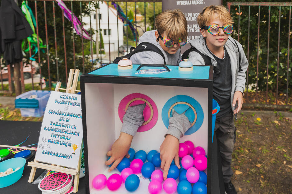na zdjęciu dwóch chłopców w śmiesznych goglach na oczach wkłada ręce do pudła z kolorowymi kulkami