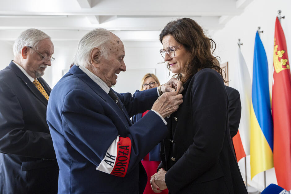 Starszy mężczyzna przypina młodszej kobiecie order.