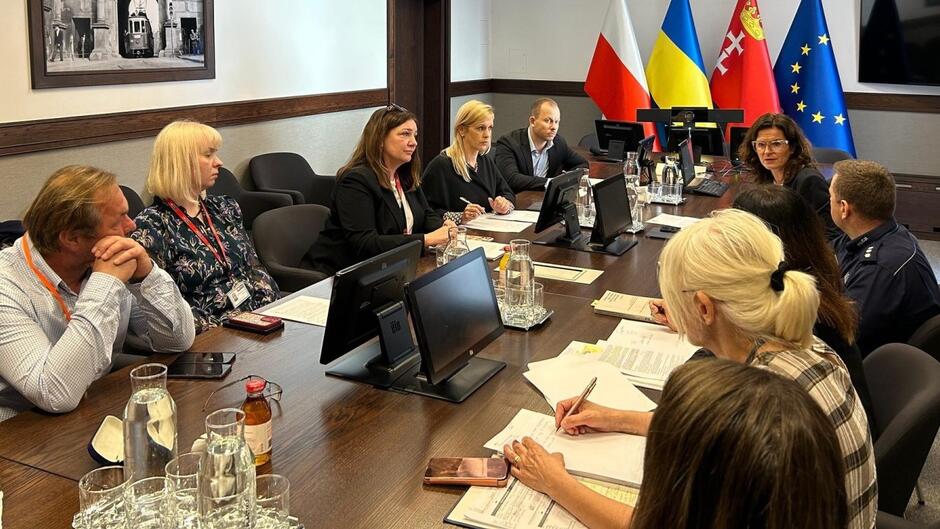 Około 10 osób, które obradują siedząc wokół dużego stołu