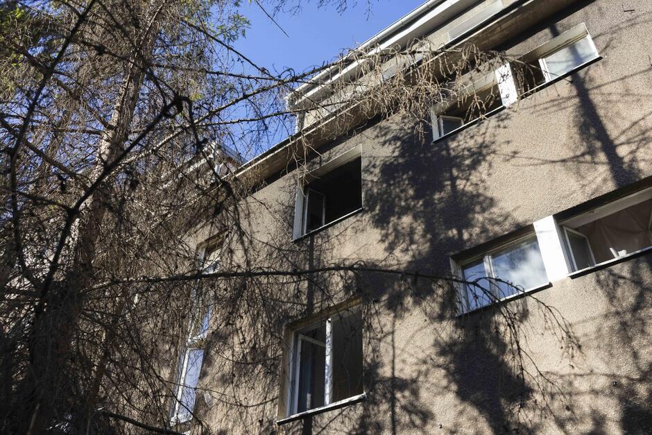 Widok budynku zrobiony z perspektywy chodnika, na górze widać otwarte okno ze śladami po pożarze 