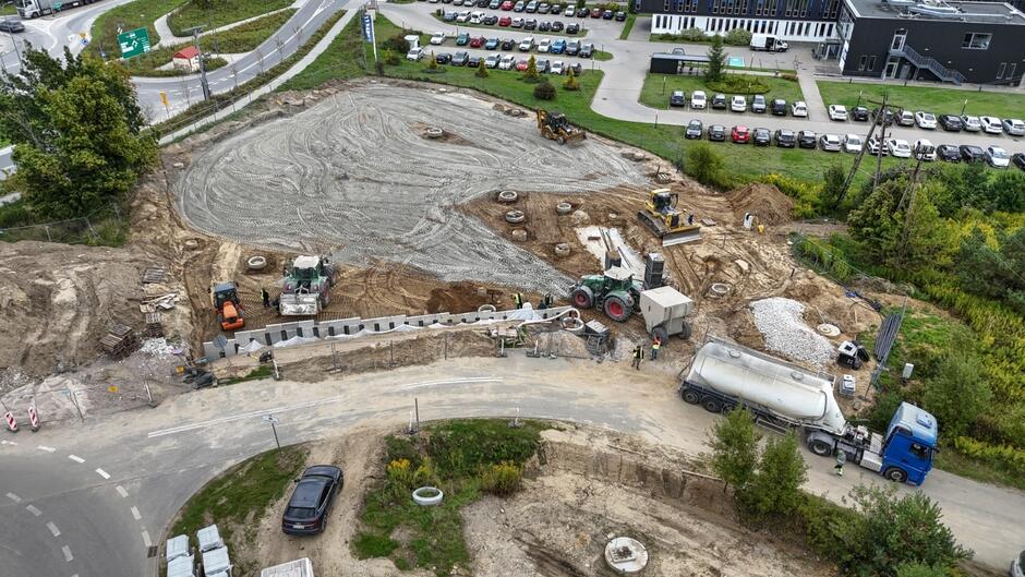 zdjęcie z drona, widać duży rozkopany teren i pracujące na nim koparki i ciężarówki